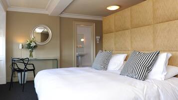 A hotel room with a large bed, a desk with a chair, a mirror, and a bathroom door.