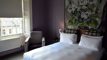 A hotel room with a bed, a chair, a radiator, and a window with blinds.