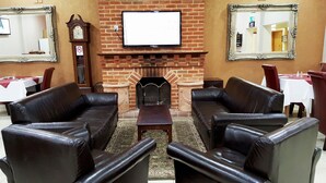 A room with leather sofas arranged around a fireplace, a clock, and a television on the wall. - Skylark Hotel (Southend-on-Sea)