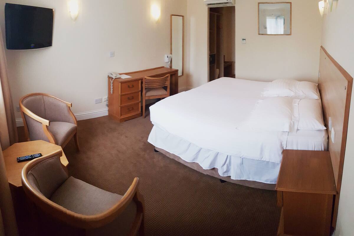 A hotel room with a large bed, a desk with a chair, a television, and a wardrobe.