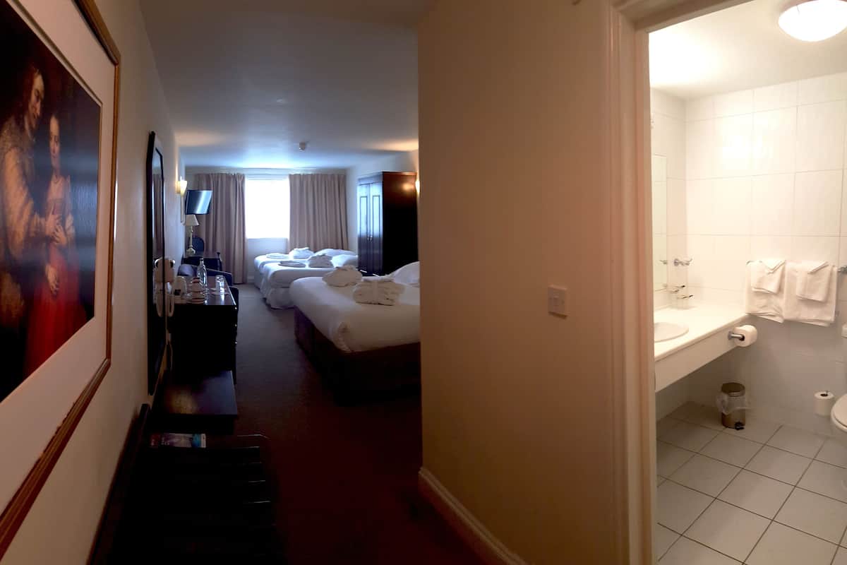 A hotel room with a bed, a desk with a lamp, a TV, and a bathroom with a sink and toilet.