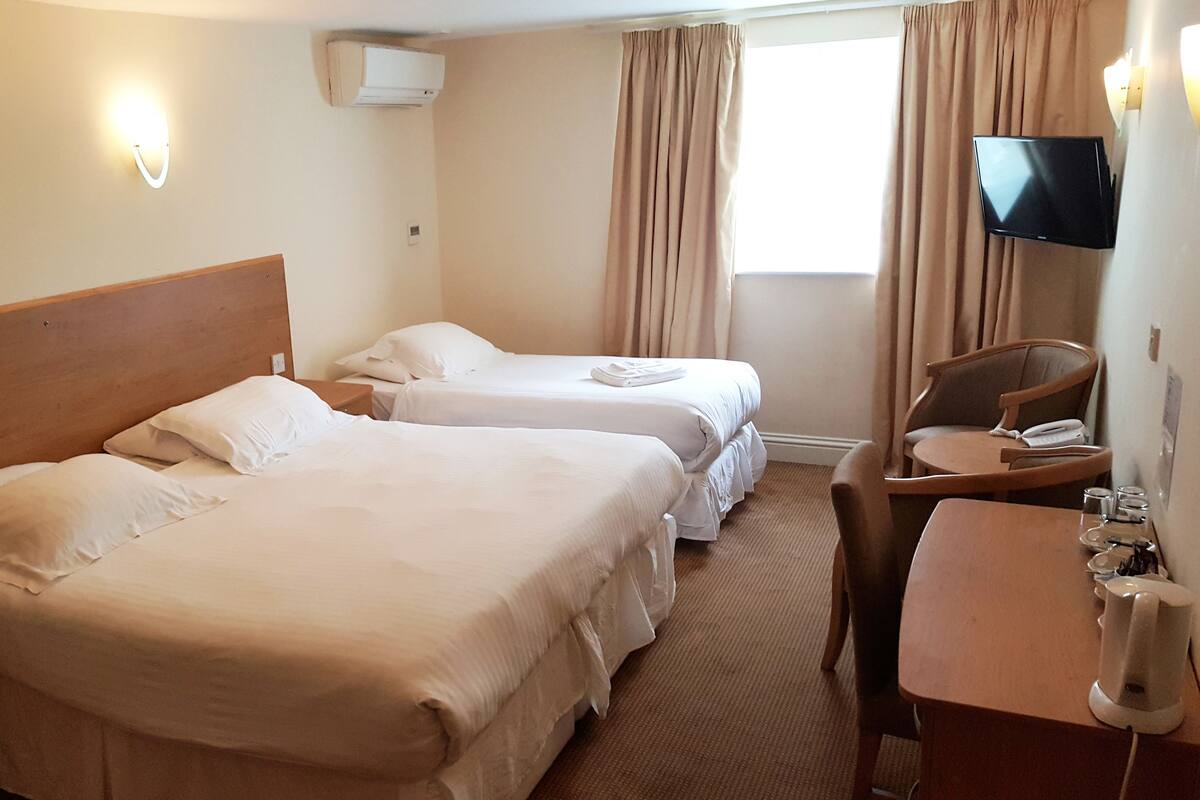 A hotel room with two beds, a desk, a chair, a TV, and a window with curtains.