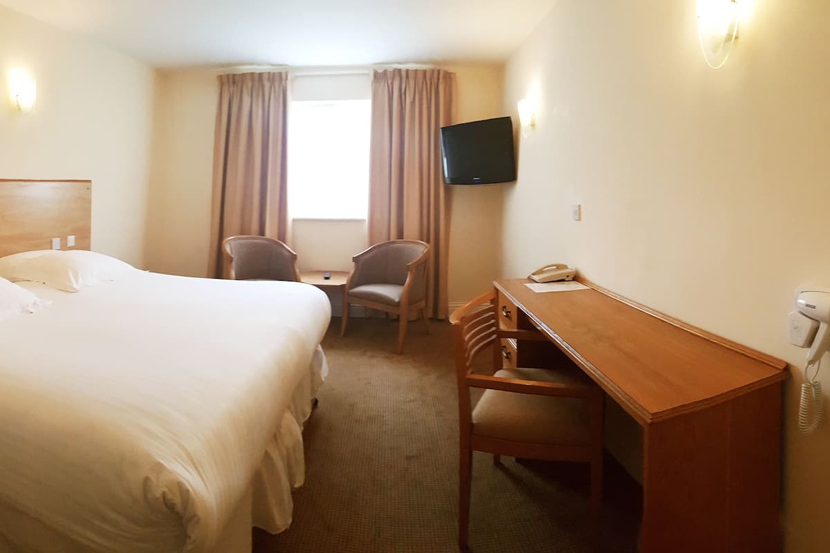 A hotel room with a double bed, a desk with a chair, a television, and a window with curtains.
