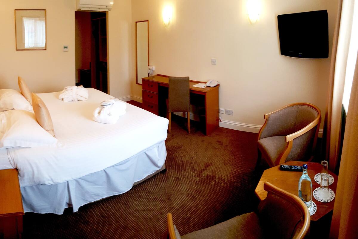 A hotel room with a bed, a desk, a chair, a television, and a minibar.