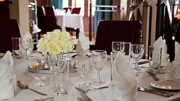 A dining table set with white napkins, silverware, and a centerpiece of white flowers. - Skylark Hotel (Southend-on-Sea)