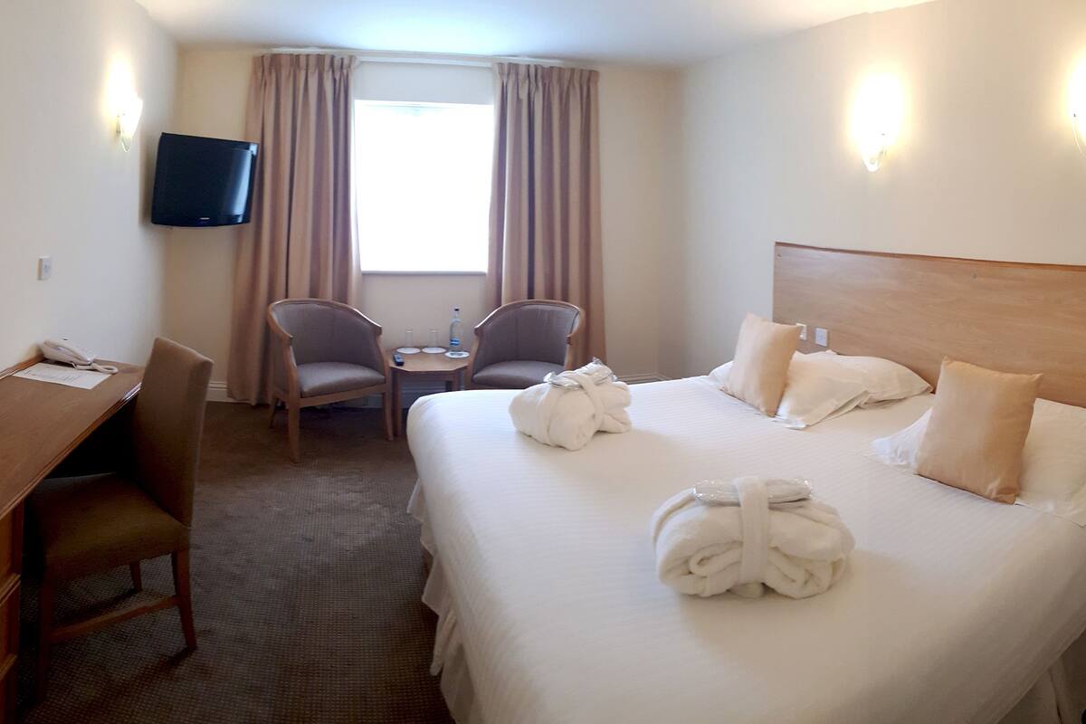 A hotel room with a bed, a desk, a chair, a TV, and a window with curtains.