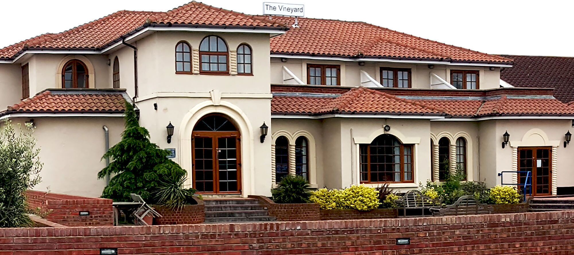 A two-story house with a red-tiled roof, multiple windows, and a brick entrance.