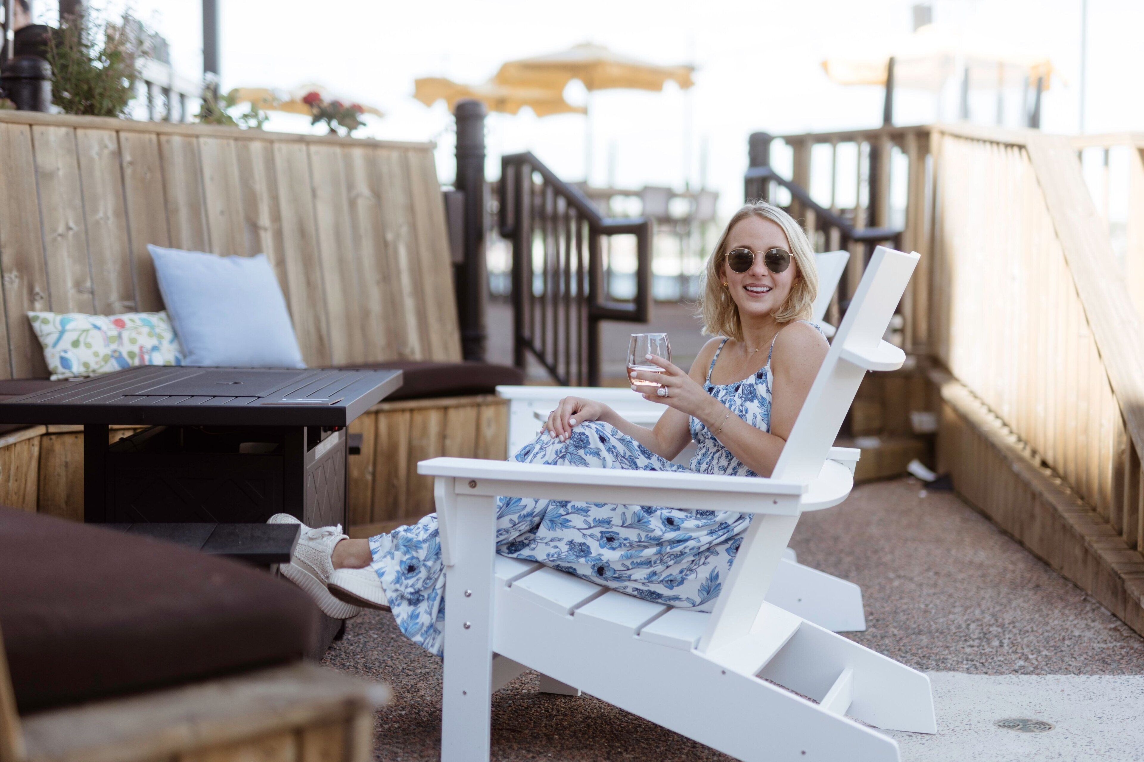A person sitting on a white outdoor chair with a table in front, a wooden deck, and a wooden fence in the background.