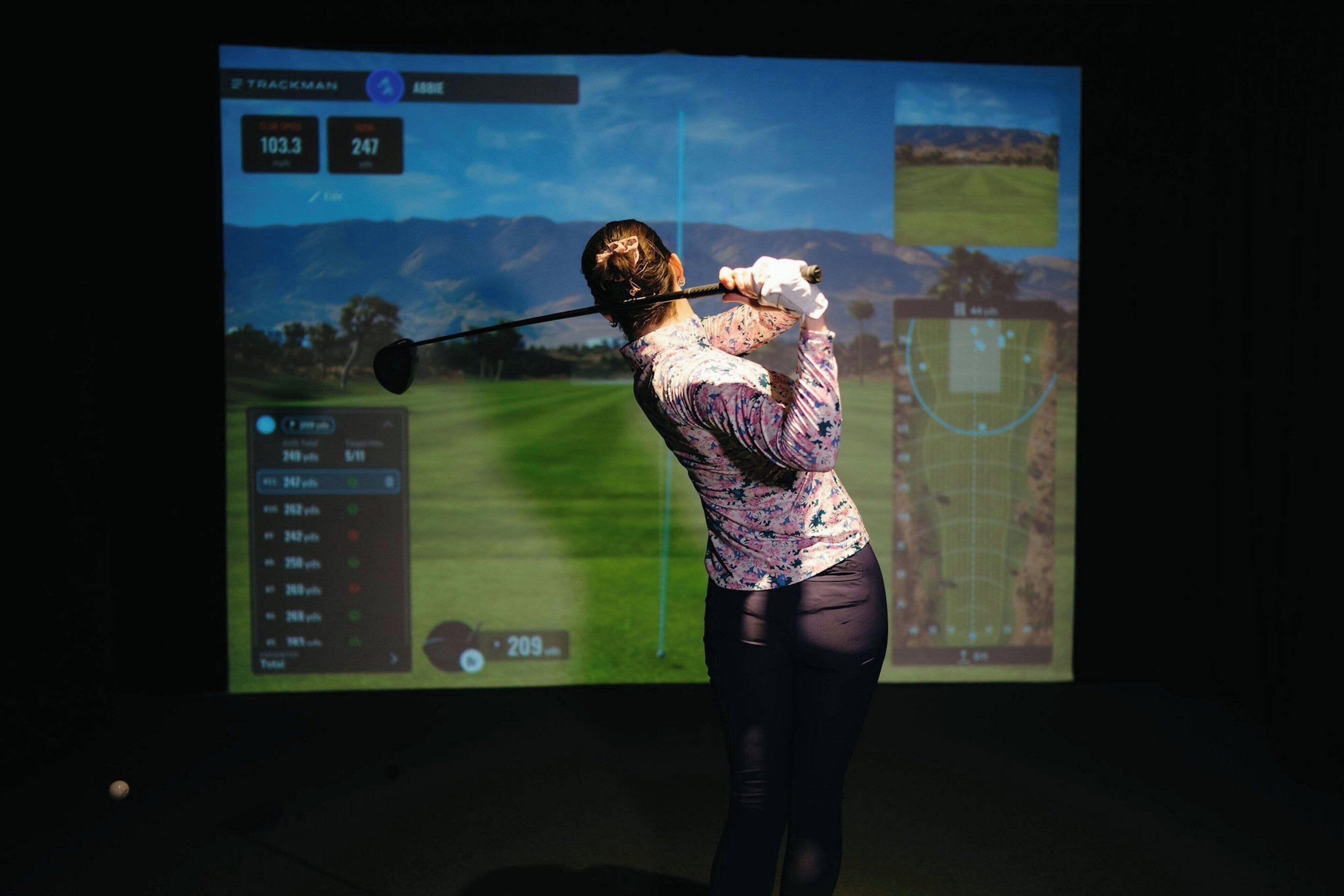 A person playing golf with a screen displaying a golf course and statistics.
