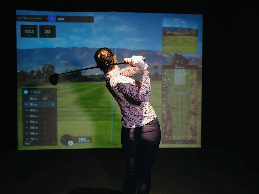 A person playing golf with a screen displaying a golf course and statistics.