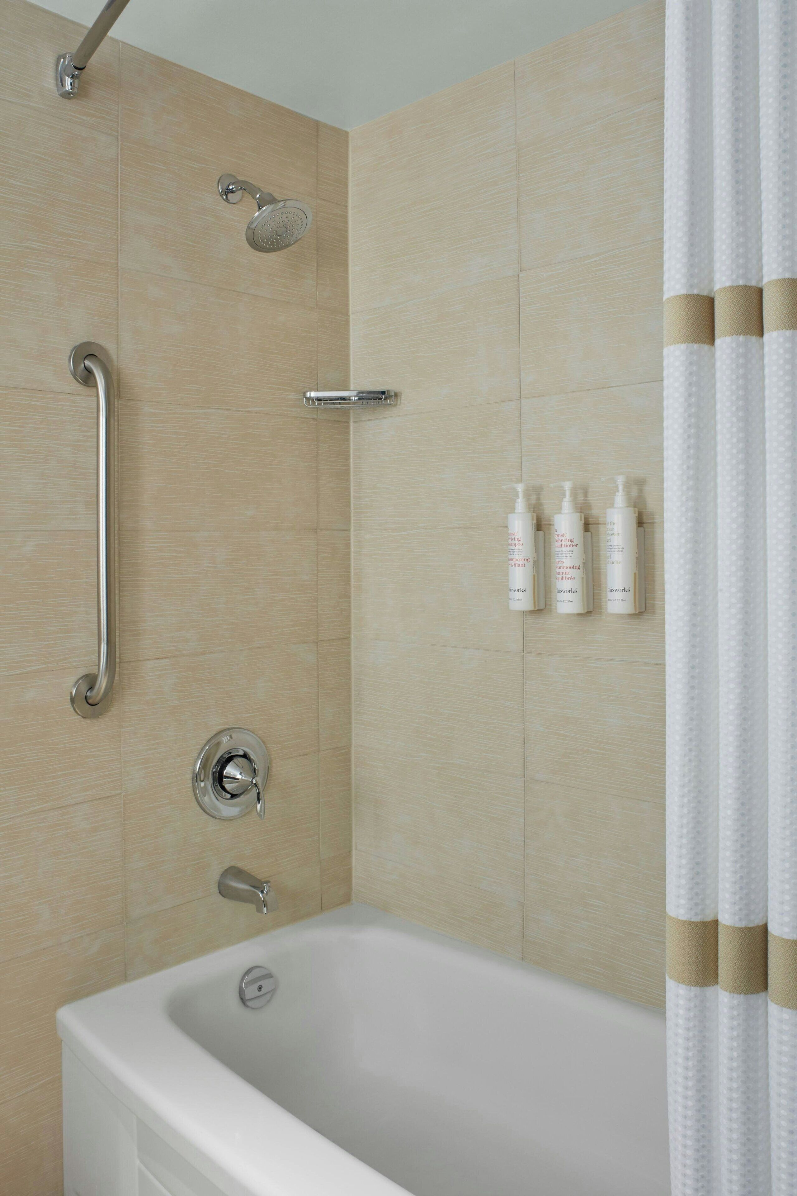 A modern bathroom with a bathtub, a shower with a handheld showerhead, a grab bar, and a set of toiletries on the wall.