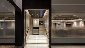 A modern hotel lobby with a staircase leading to the club area, glass walls, and a clean, contemporary design.