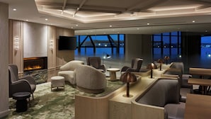 A modern hotel lobby with a fireplace, comfortable seating, a bar area, and large windows offering a view of the cityscape.