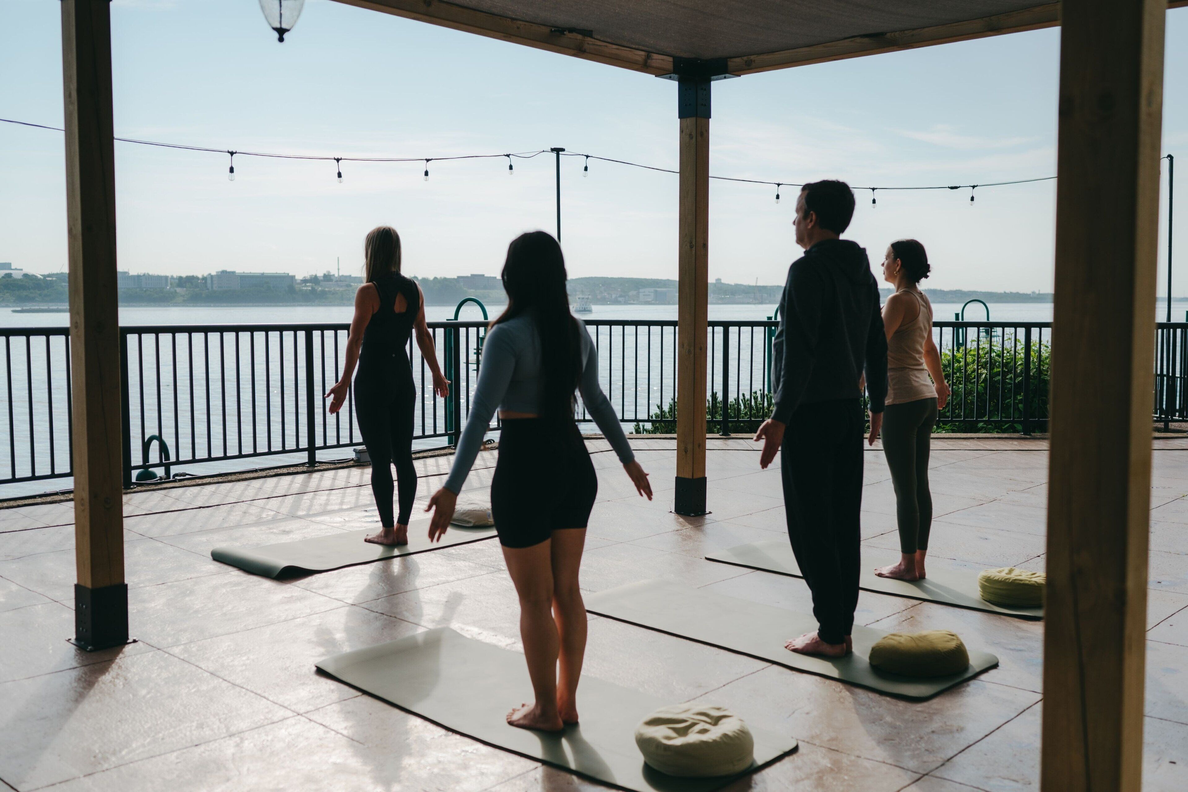 Un gruppo di persone che pratica yoga su tappetini all'aperto, con vista su un'area acquatica e sullo skyline della città sullo sfondo.