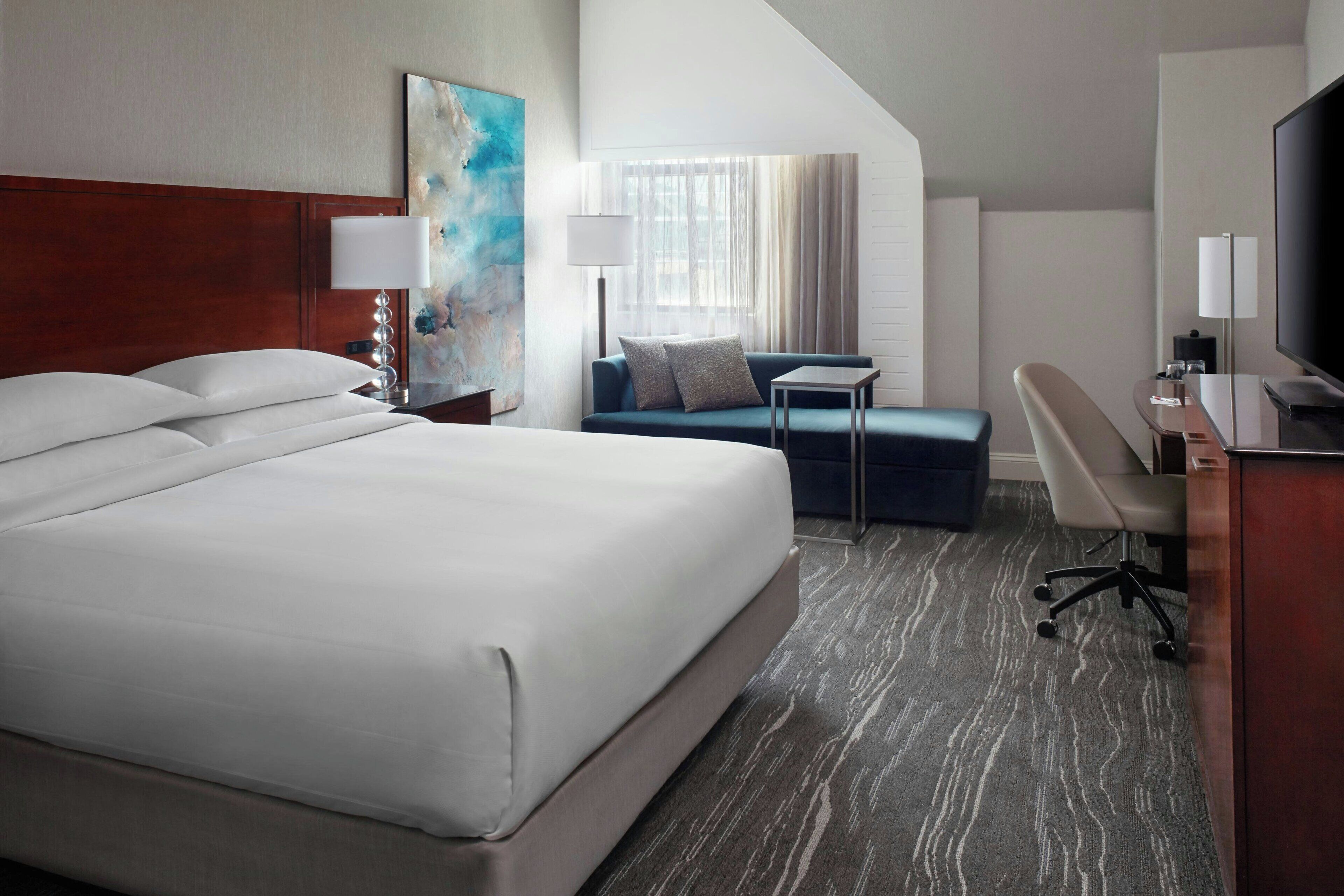 A hotel room with a large bed, a desk, a chair, a sofa, and a television.