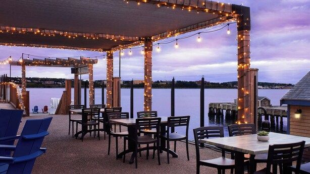 An outdoor dining area with tables and chairs, string lights, and a view of the water.