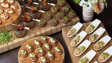 Diversos aperitivos dispuestos sobre tablas de madera y en frascos de vidrio, con un jarrón de flores al fondo.