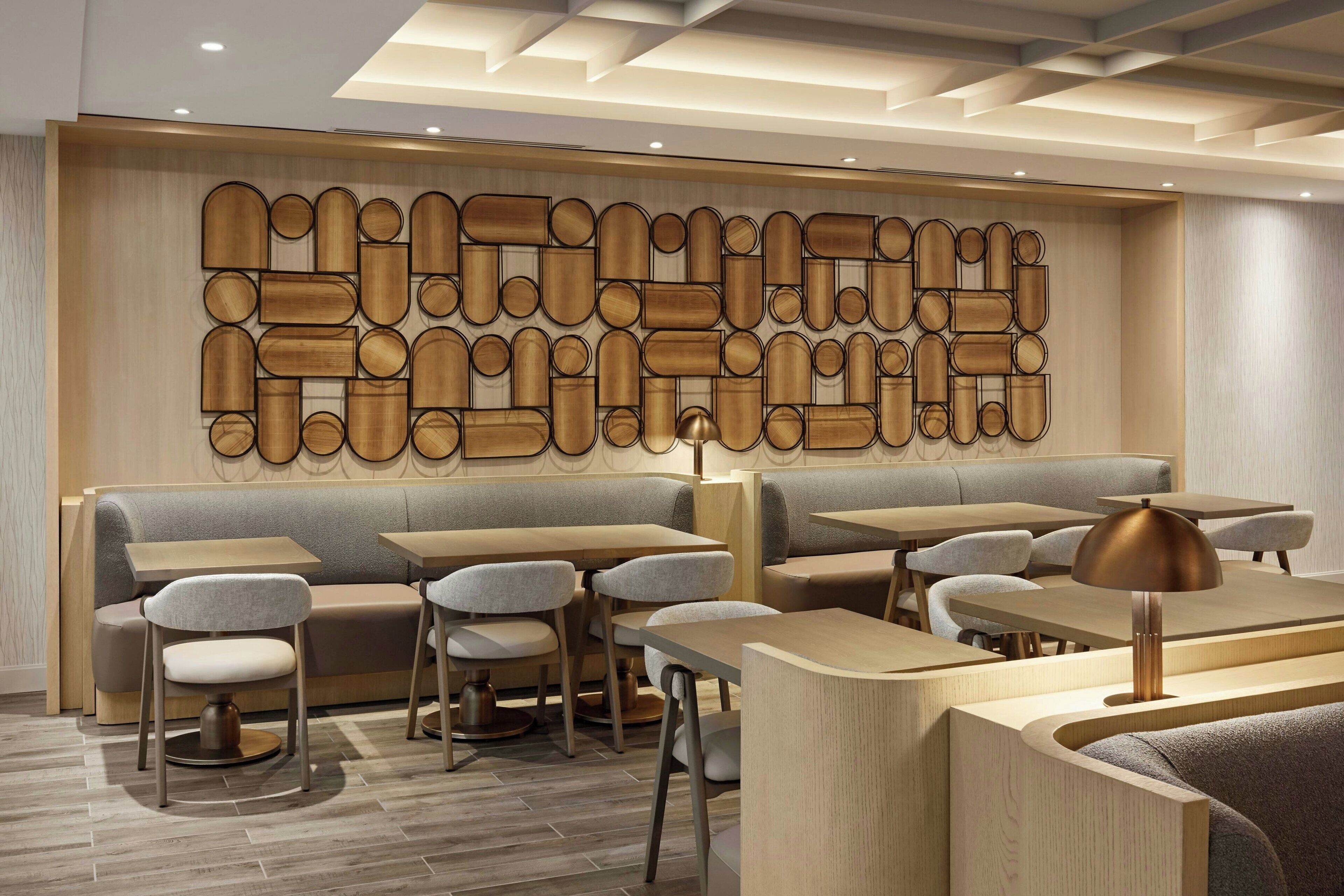 A modern restaurant interior with a wooden wall art installation, cushioned seating, and contemporary tables.