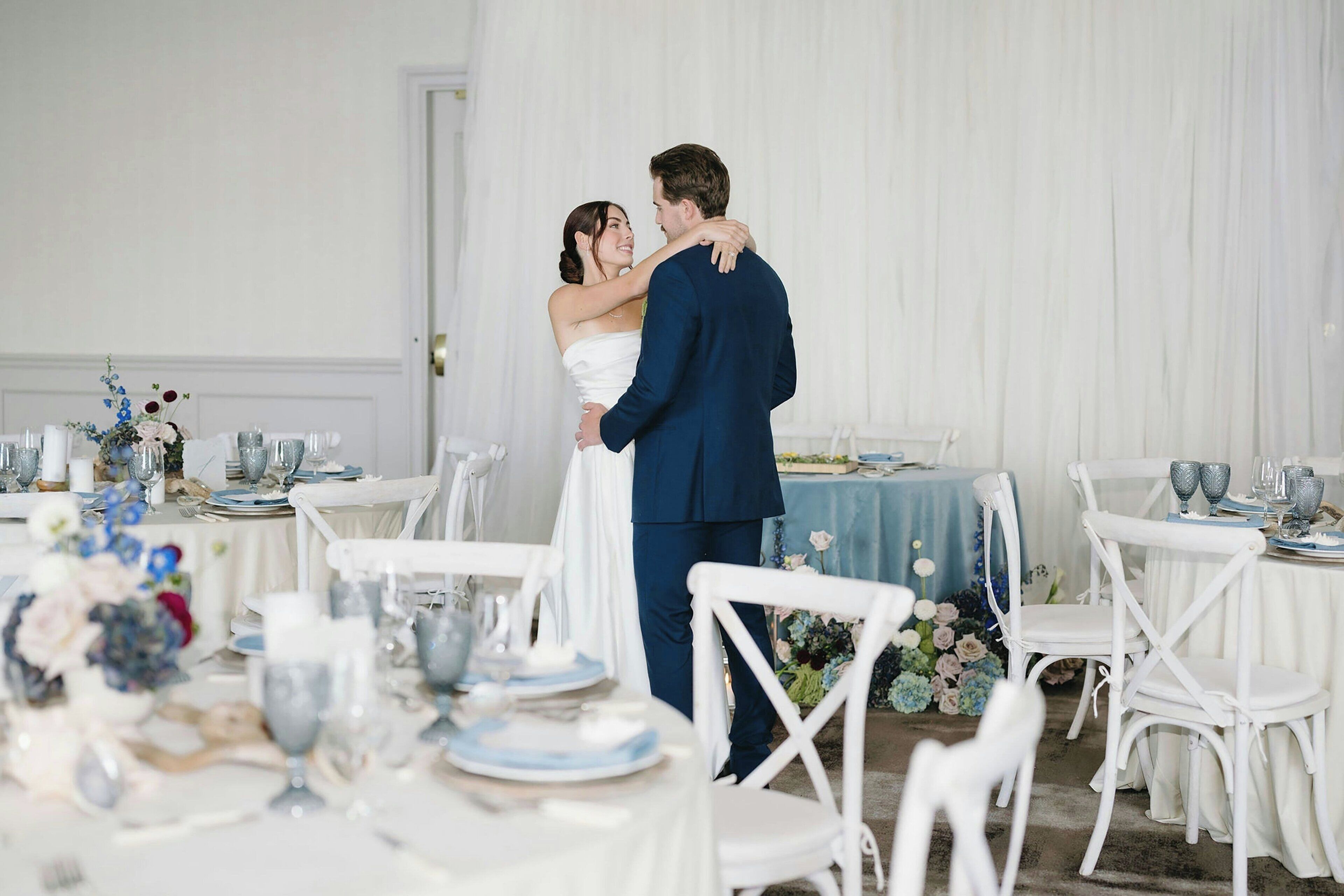 A wedding reception with white tables and chairs, floral centerpieces, and a white backdrop.