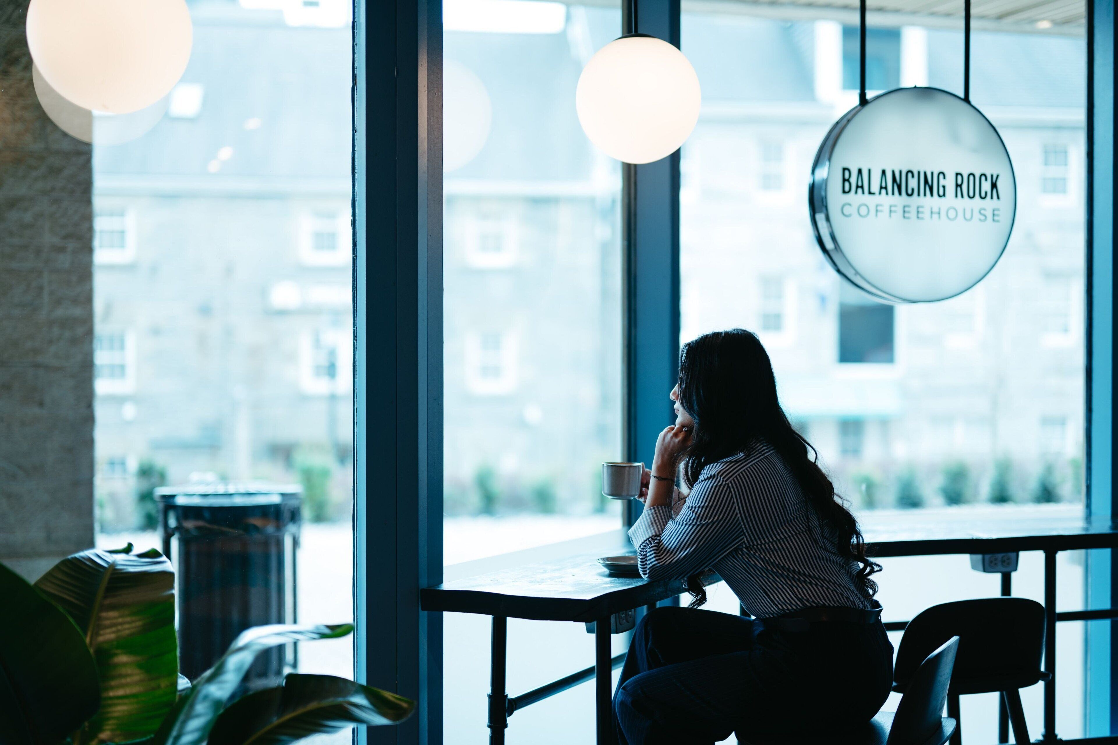 A person sitting at a table in a cafe with a view of buildings outside.