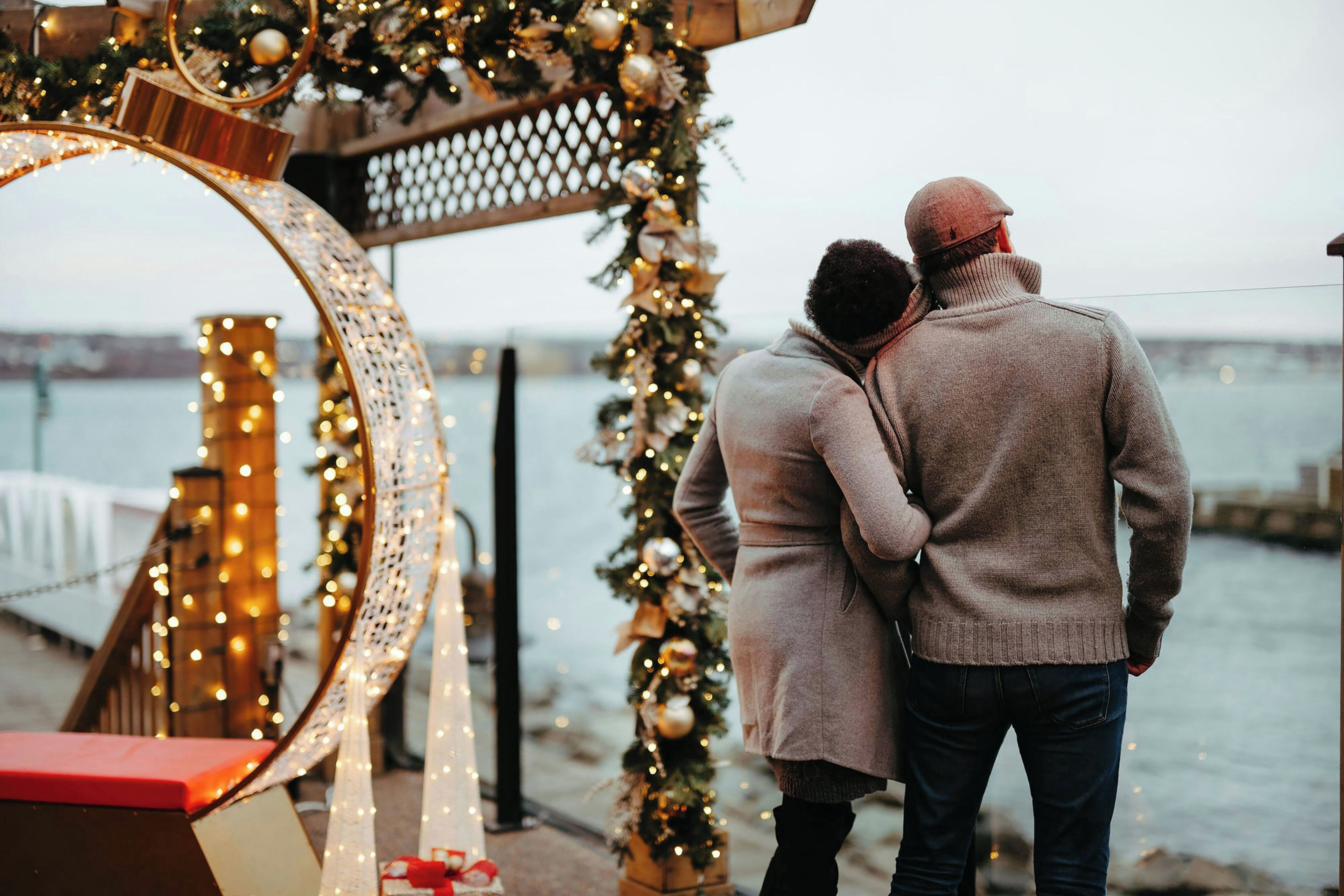 A couple embracing under a decorated archway with a view of a body of water.