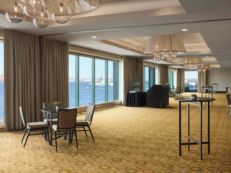 Ein Hotelzimmer mit großen Fenstern, einem gemusterten Teppich und einem Essbereich mit Stühlen und Tischen.
