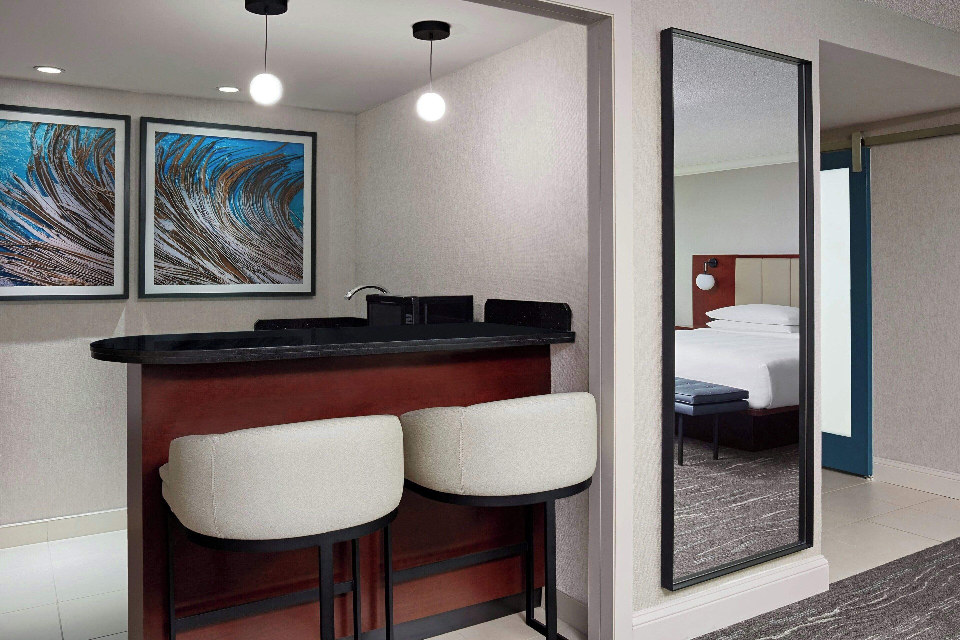 A hotel room with a bar area, two framed artworks, a large mirror, and a bed with a blue accent wall.