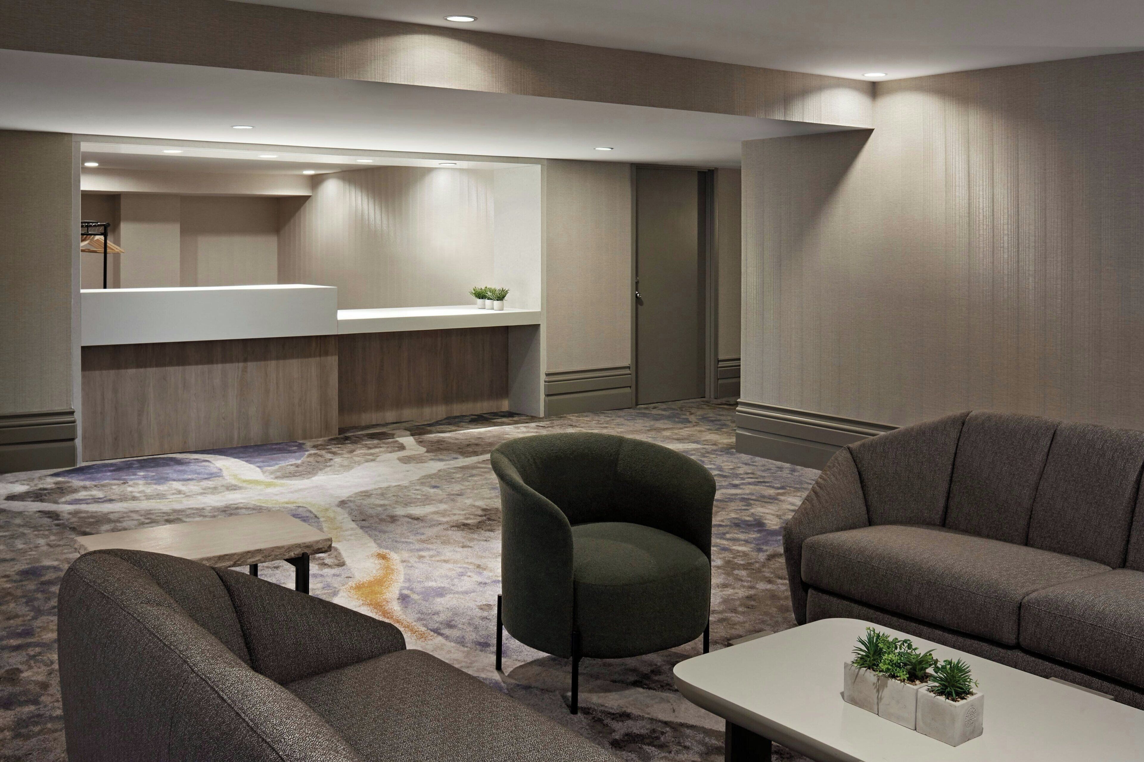 A modern hotel lobby with a carpeted floor, a reception desk, and seating areas.