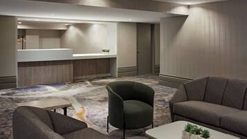 A modern hotel lobby with a carpeted floor, a reception desk, and seating areas.
