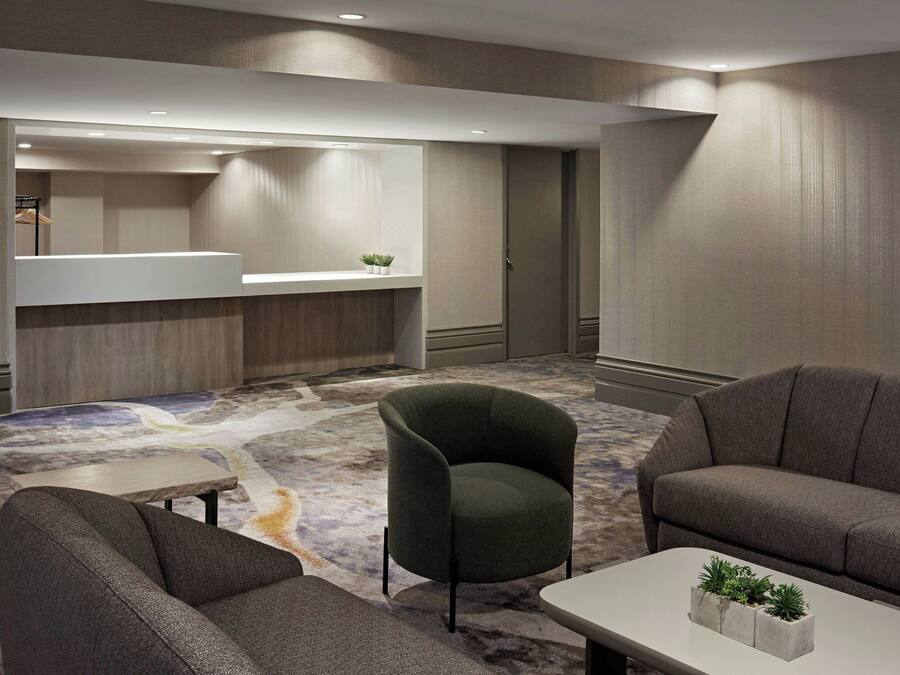 A modern hotel lobby with a carpeted floor, a reception desk, and seating areas.