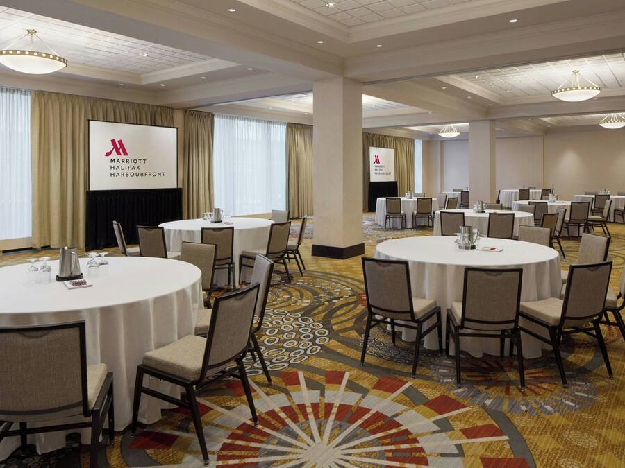 A hotel conference room with round tables, chairs, and a large screen displaying the hotel's logo.