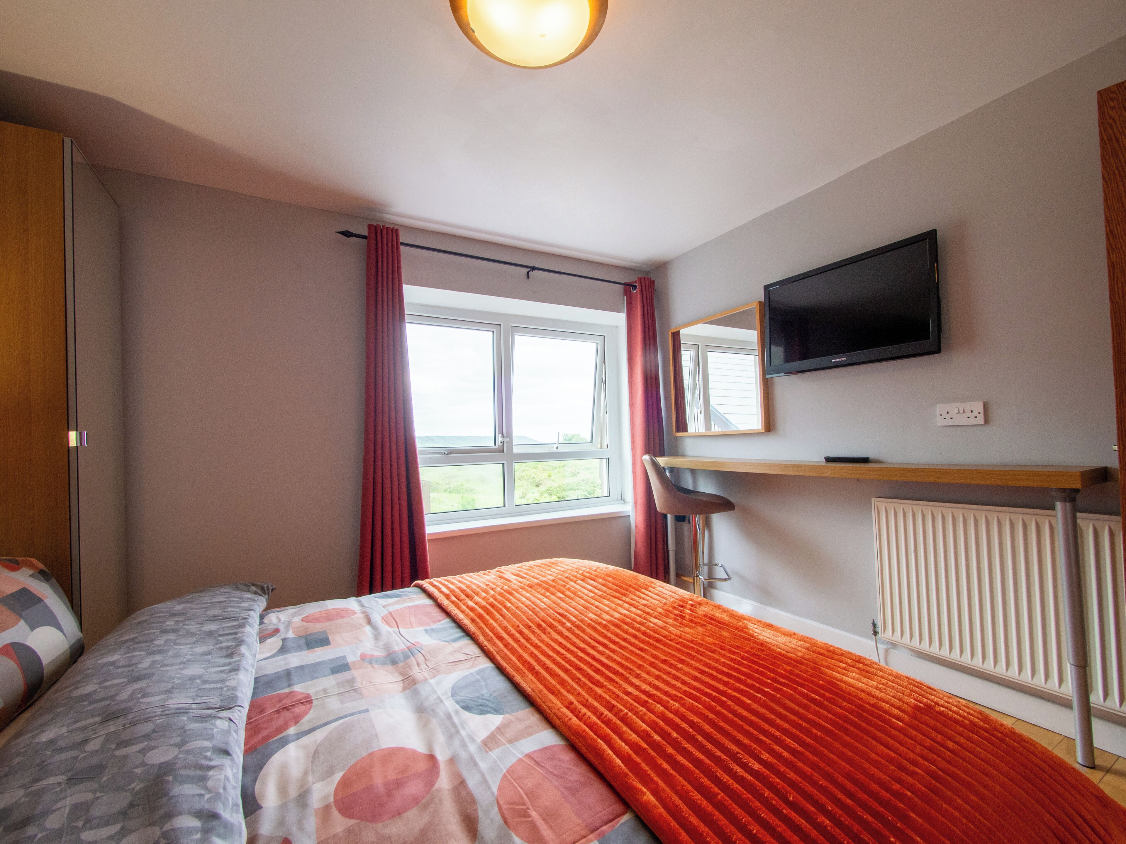 A bedroom with a bed, a window with curtains, a television, and a radiator.