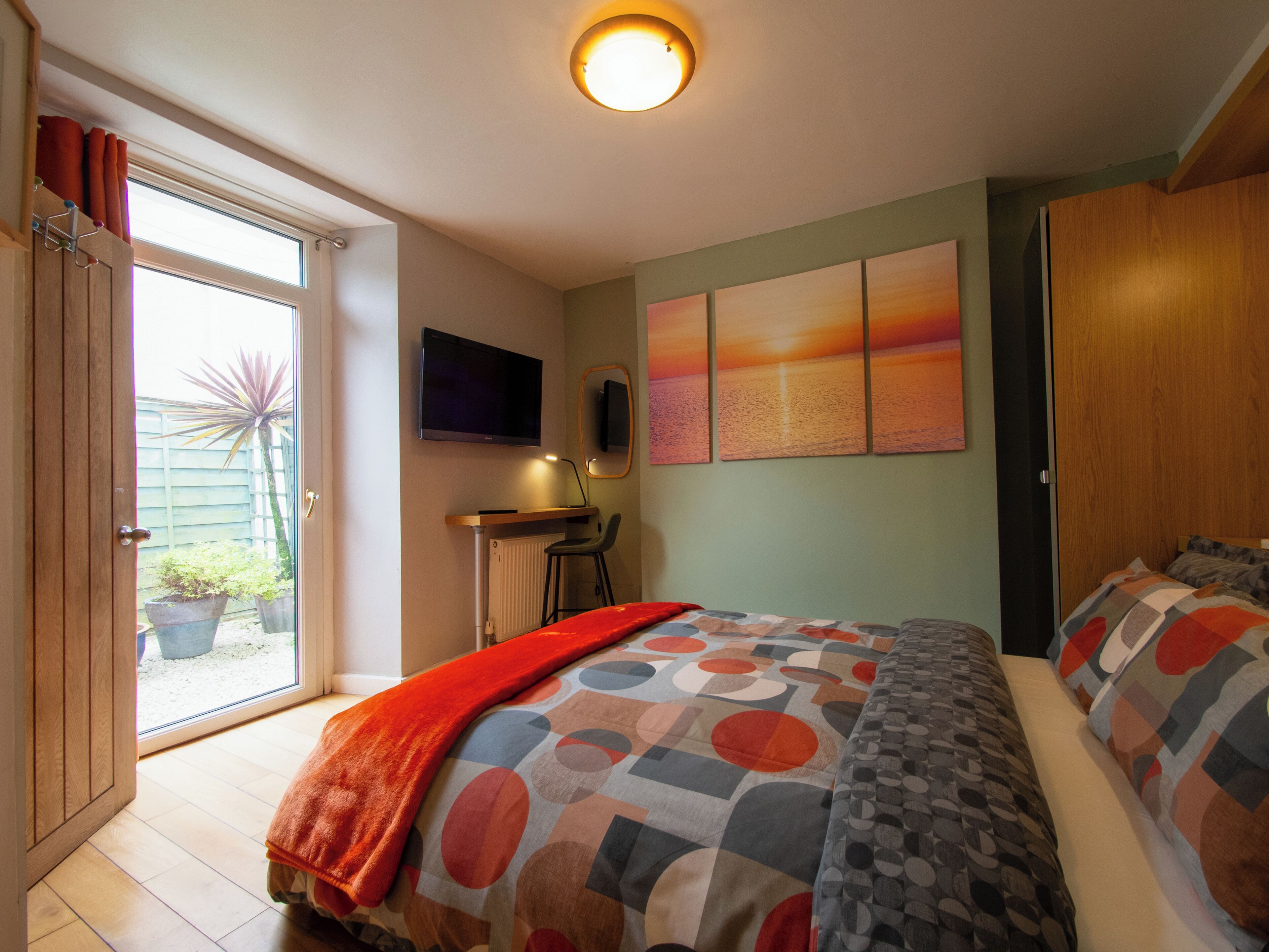 A bedroom with a bed, a desk, a chair, a television, and a view of the outside.