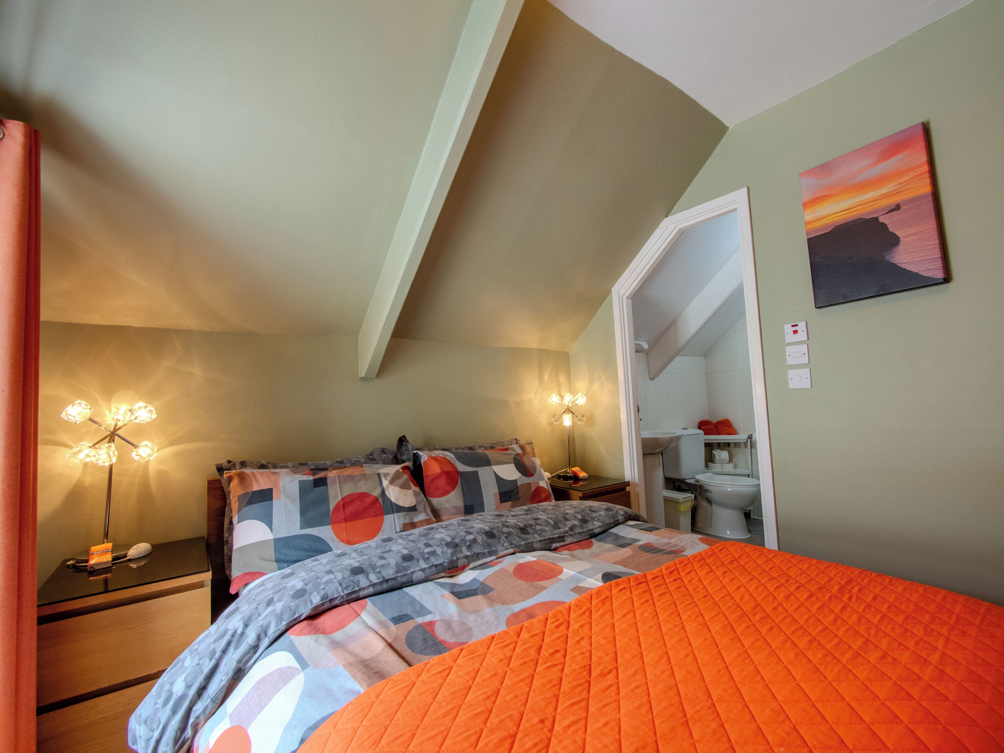 A bedroom with a bed, bedside tables, a nightstand, a lamp, and a painting on the wall.