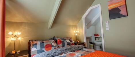 A bedroom with a bed, bedside tables, a nightstand, a lamp, and a painting on the wall.