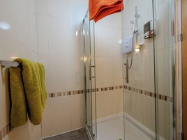 A glass-enclosed shower stall with a handheld showerhead, a towel rack with two towels, and a wall-mounted control panel.