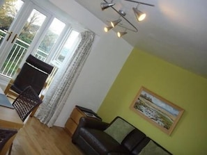 Una habitación con piso de madera, un sofá de cuero negro, una mesa de comedor con sillas, una mesita auxiliar y un cuadro en la pared.