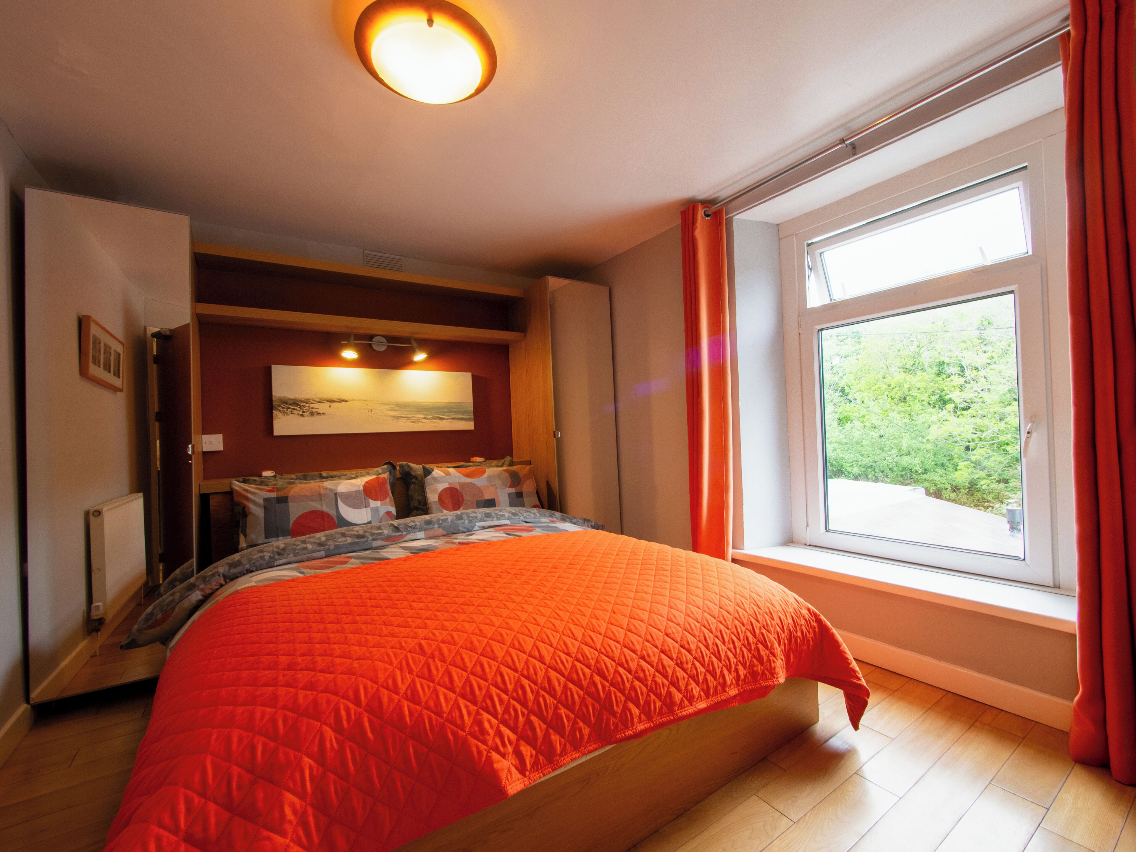 Une chambre à coucher avec un lit, une fenêtre avec des rideaux, un tableau au mur et un luminaire au plafond.