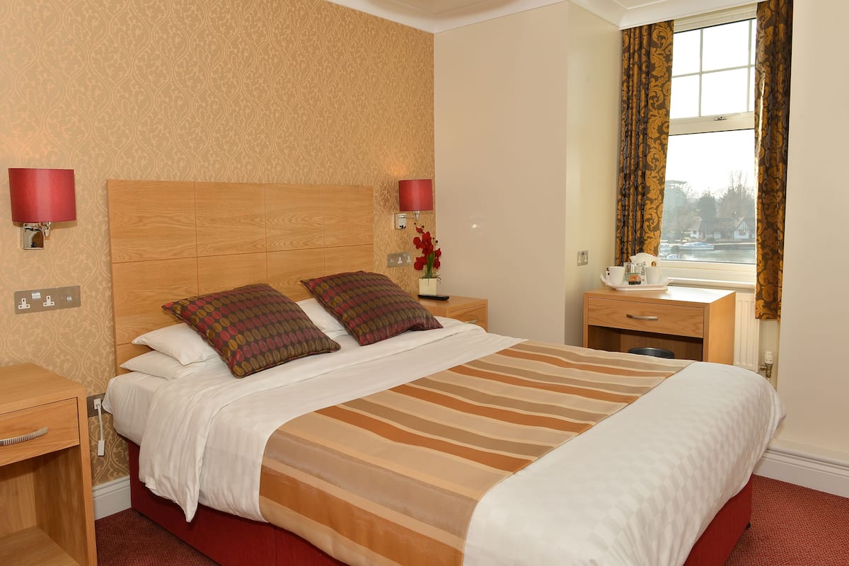 A neatly made bed with a striped bedspread, two pillows, a nightstand with a lamp, and a window with curtains.
