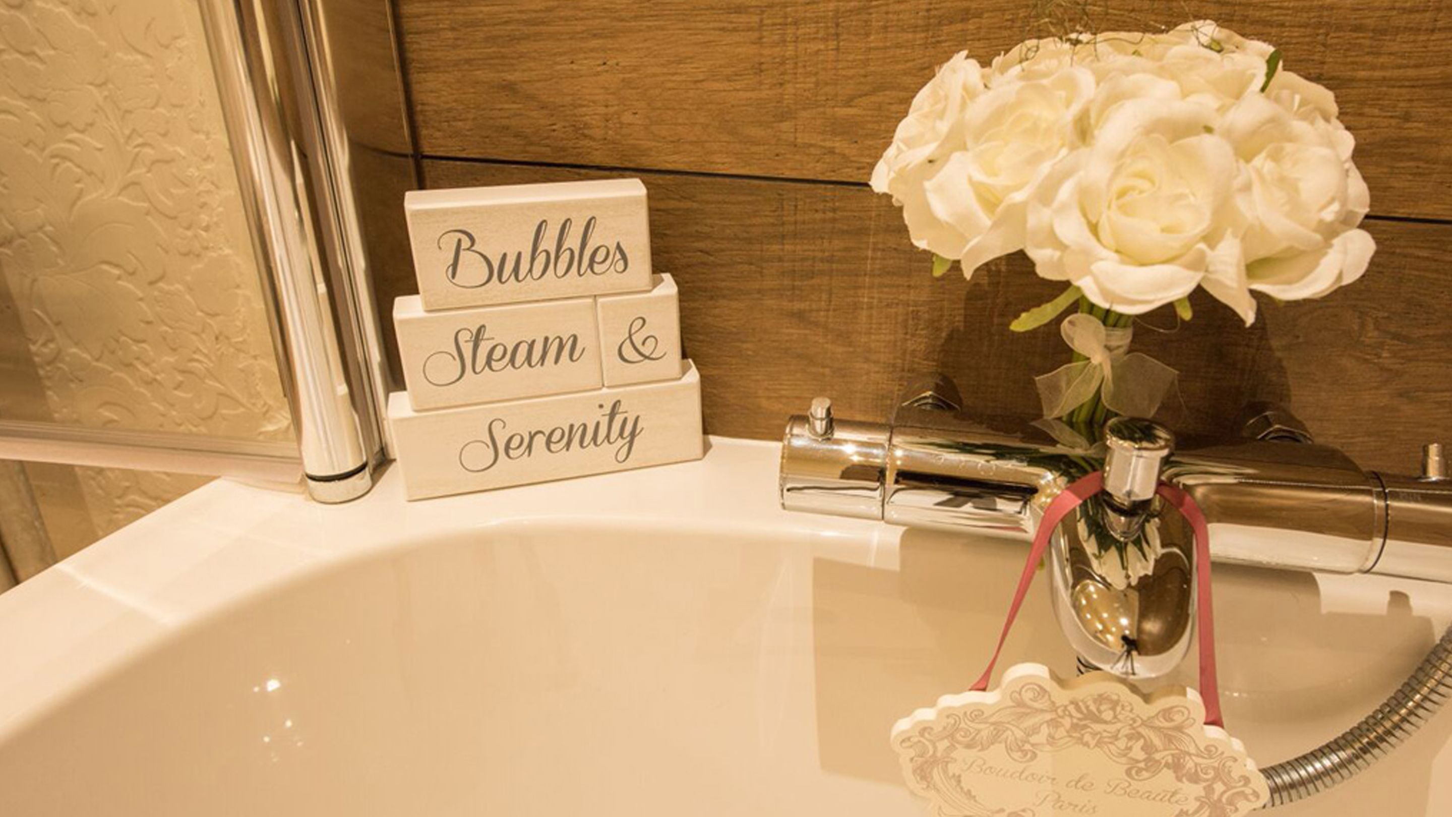 A bathroom sink with a floral arrangement and a sign that reads "Bubbles Steam & Serenity".