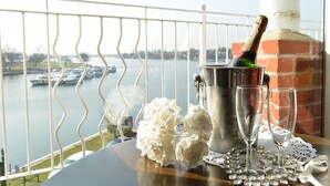A balcony with a view of a lake and boats, a metal bucket with a bottle, two glasses, and decorative flowers on a table. - Wherry Hotel (Lowestoft)