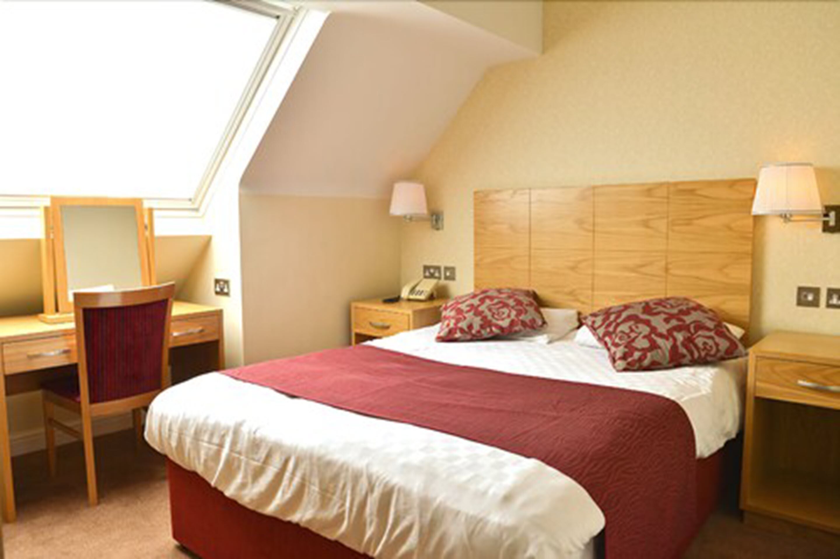 Een slaapkamer met een bed, een bureau, een stoel, een nachtkastje en een lamp.