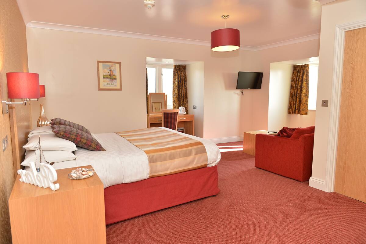 A hotel room with a bed, a desk, a red sofa, a TV, and a red carpet.
