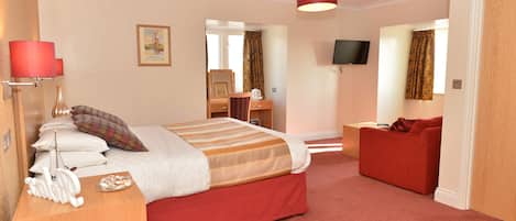 Quarto de hotel com cama, escrivaninha, sofá vermelho, televisão e tapete vermelho.