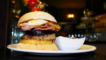 A sandwich with multiple layers of meat and egg on a bun, served on a plate with a small bowl of sauce.