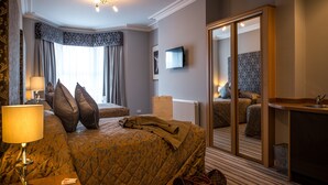 Una habitación de hotel con una cama, una mesita de noche con lámpara, un aparador, un espejo y un televisor en la pared.