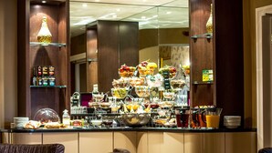 Un bufé de desayuno con diversas opciones de comida y bebidas, una zona de estar con sillas y un espejo que refleja la sala.