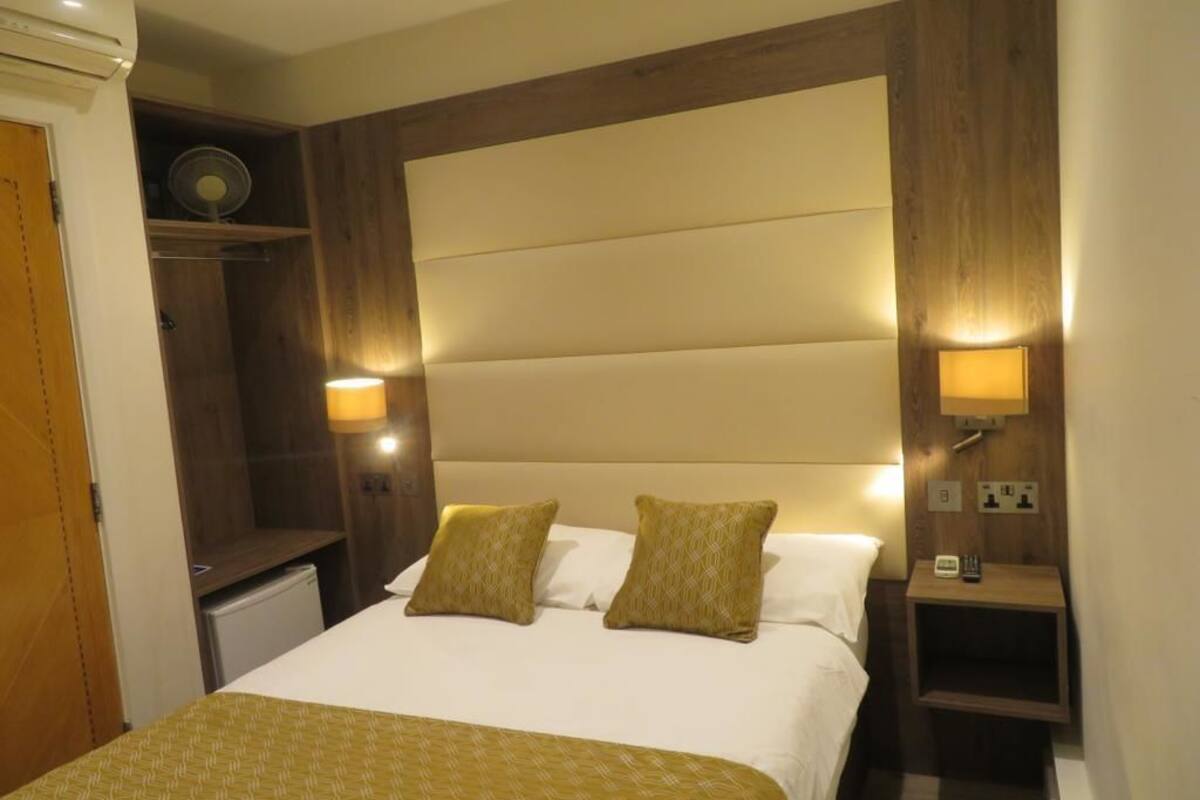 Hotellihuone, jossa on suuri sänky, kaksi yöpöytävalaisinta, puinen sängynpääty ja pieni yöpöytä.