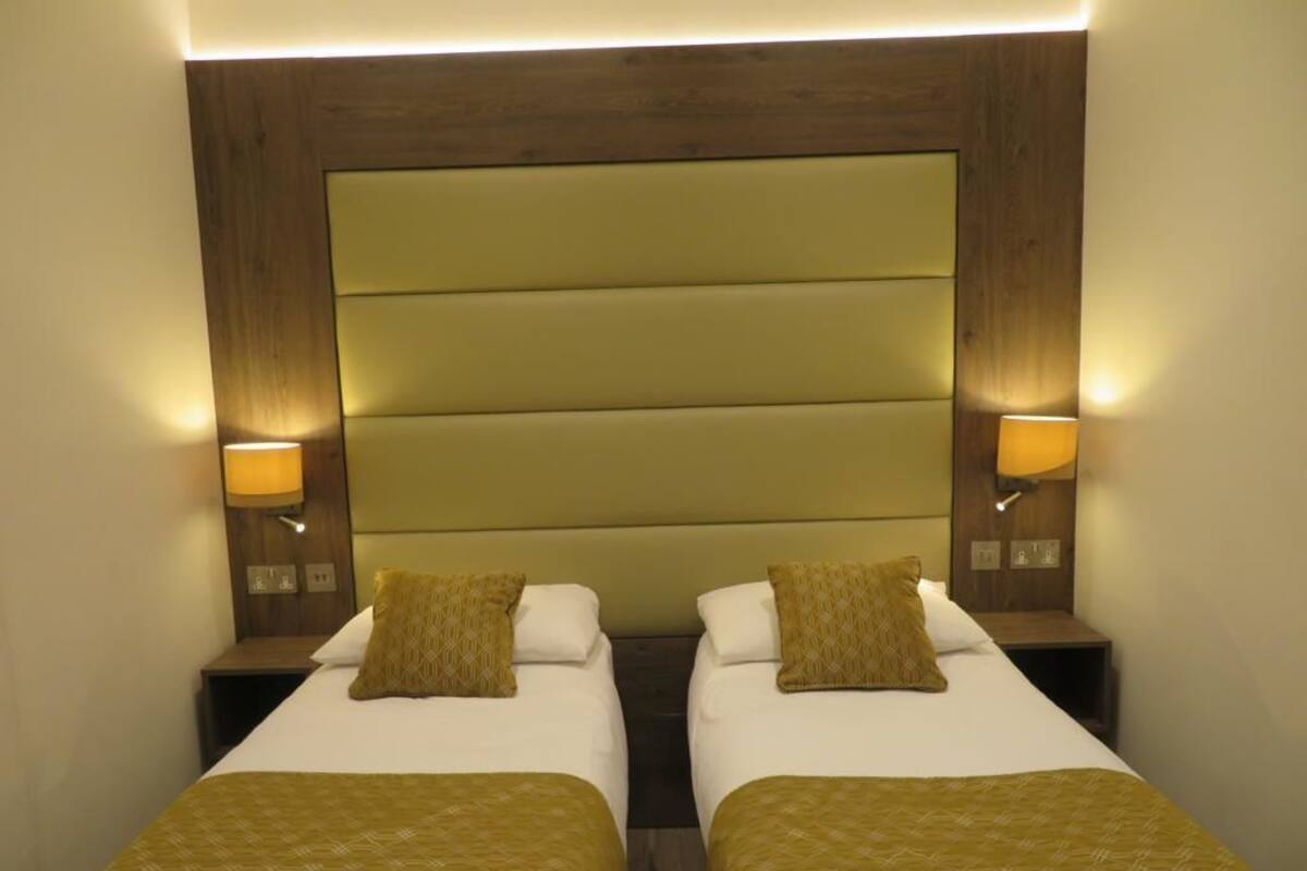 Hotellihuone, jossa on kaksi erillistä sänkyä, ja jokaisessa sängyssä on pääty, yöpöytälamppu ja samanlaiset koristetyynyt.
