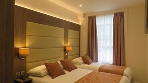 A hotel room with two beds, a wooden headboard, a nightstand, and a window with curtains.